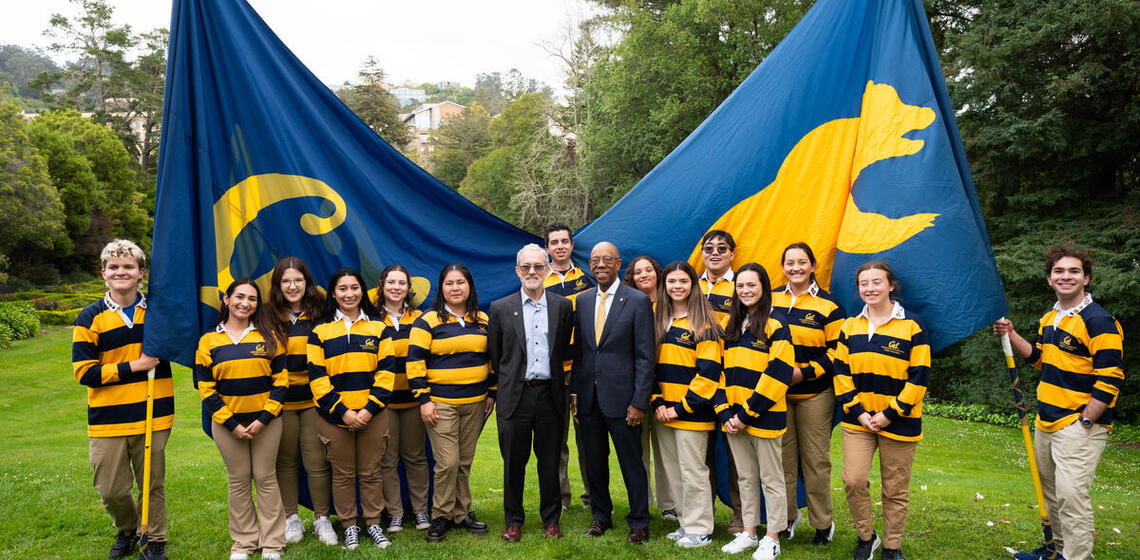 rich lyons posing with students and president drake with cal flags in the background