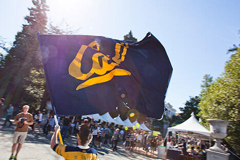 large Cal flag, held by a student in Cal gear, surrounded by other Cal students who are feeling their school spirit